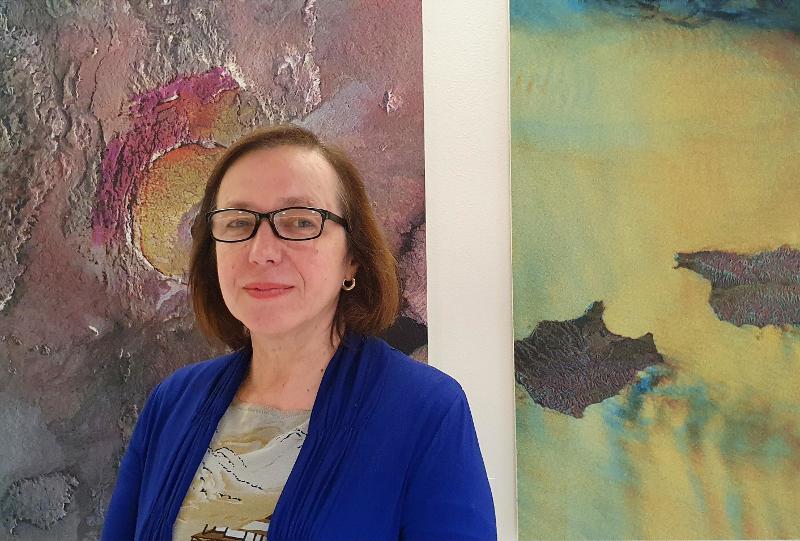 Leder av kunstutvalget ved UiT, Larissa Acharya, med bilder fra utstillingen i bakgrunnen.